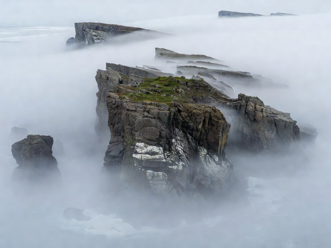 Isolated rocky Arctic island cliff emerging through dense fog